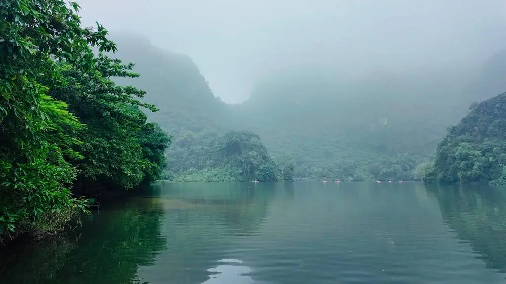 Calm water and mountains of Trang An Grottoes area covered in fog